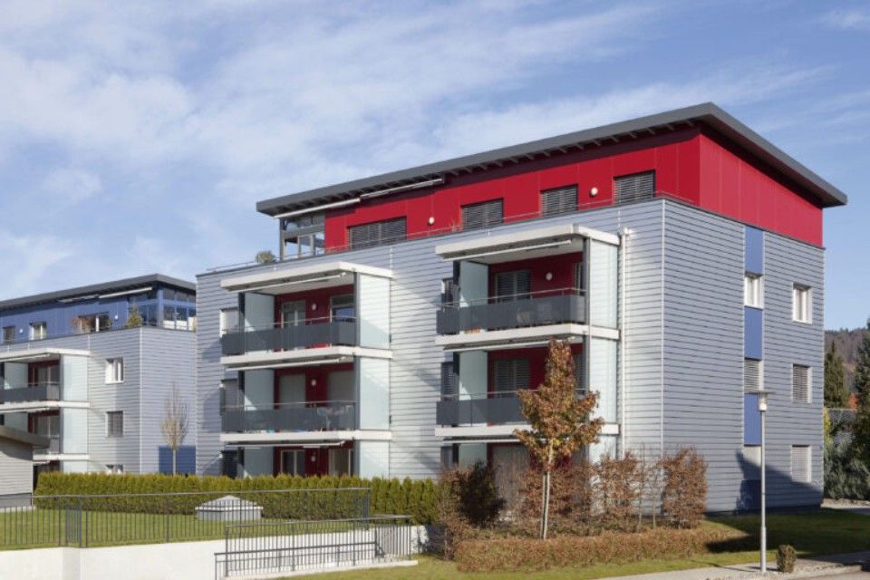 Moderne Wohnhäuser mit grauen und roten Fassaden und Balkonen an einem sonnigen Tag.