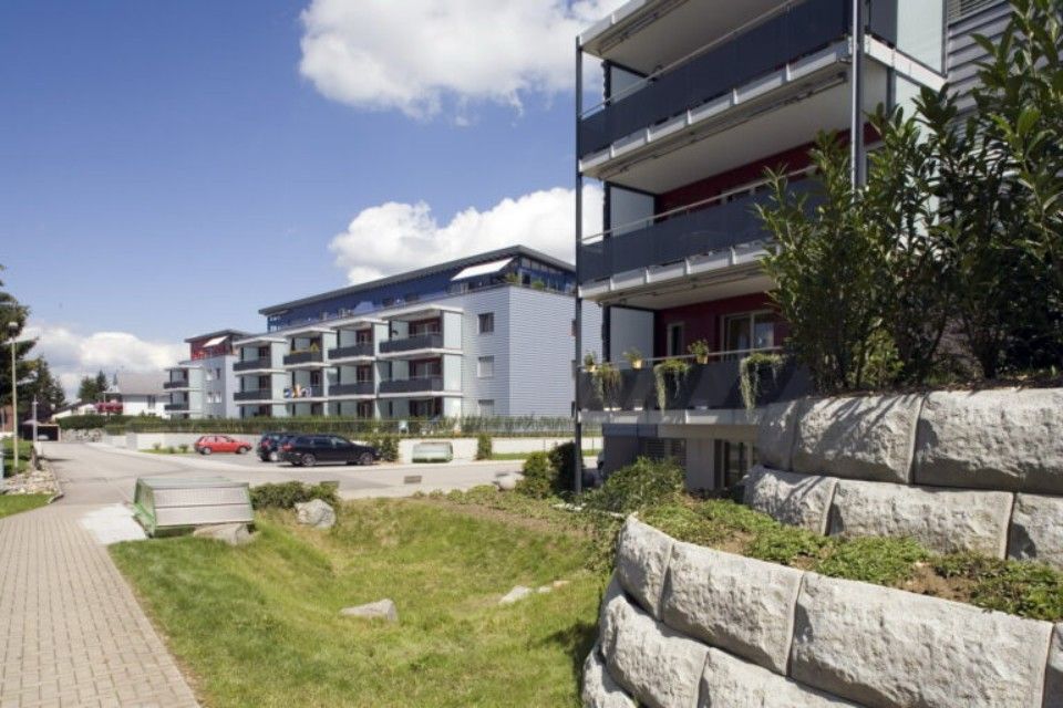 Moderne Wohngebäude mit Balkonen, grauen Wänden, blauem Himmel und einer Rasenfläche.