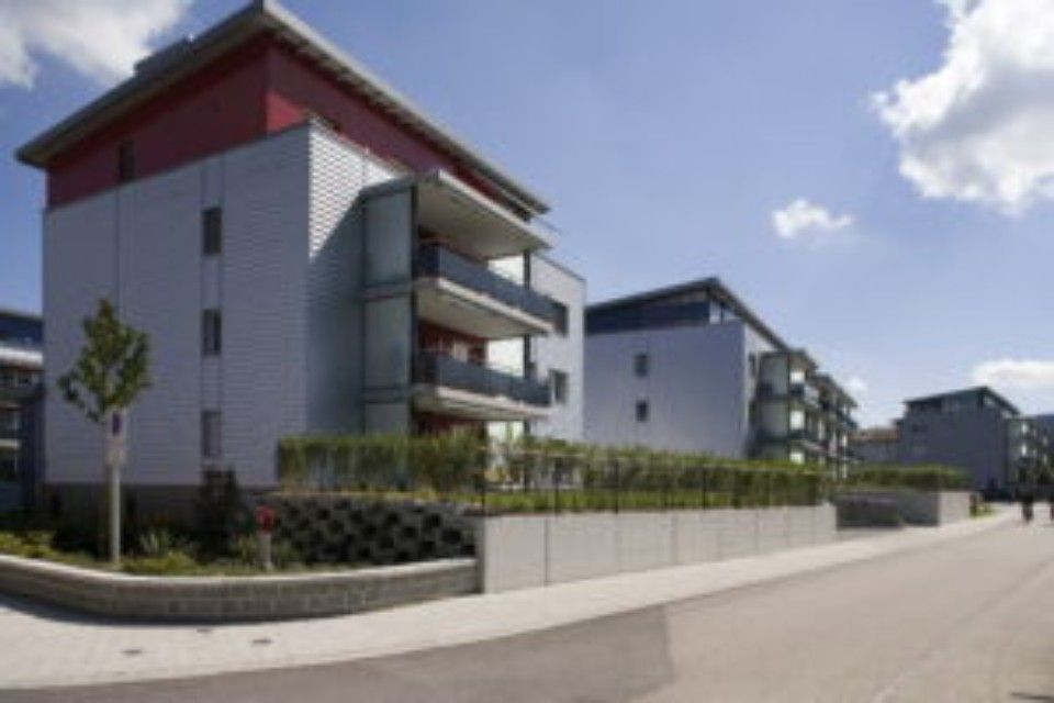 Moderne Apartmentgebäude mit silberner Fassade, roten Akzenten und Balkonen unter blauem Himmel.