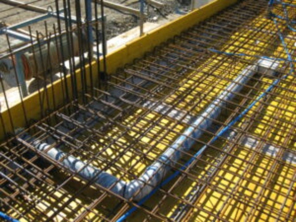 Baustelle mit in gelbe Schalung eingebettetem Bewehrungsgitter und PVC-Rohren.