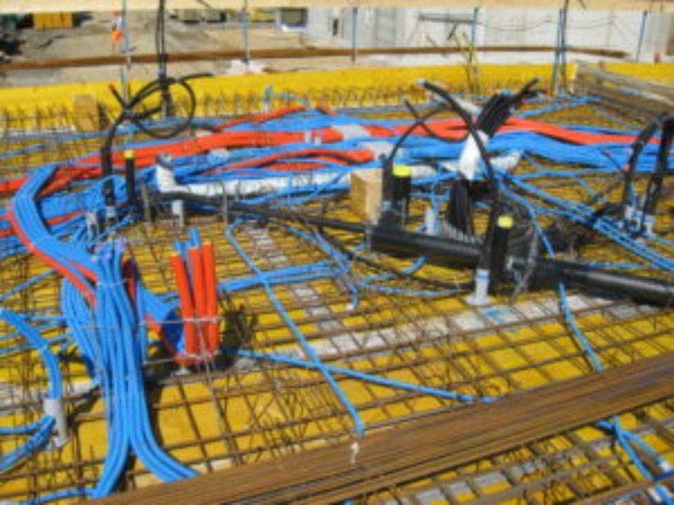 Baustelle mit blauen und orangefarbenen Leitungsrohren über einem gelben Deck, Stahlbewehrungsgitter.