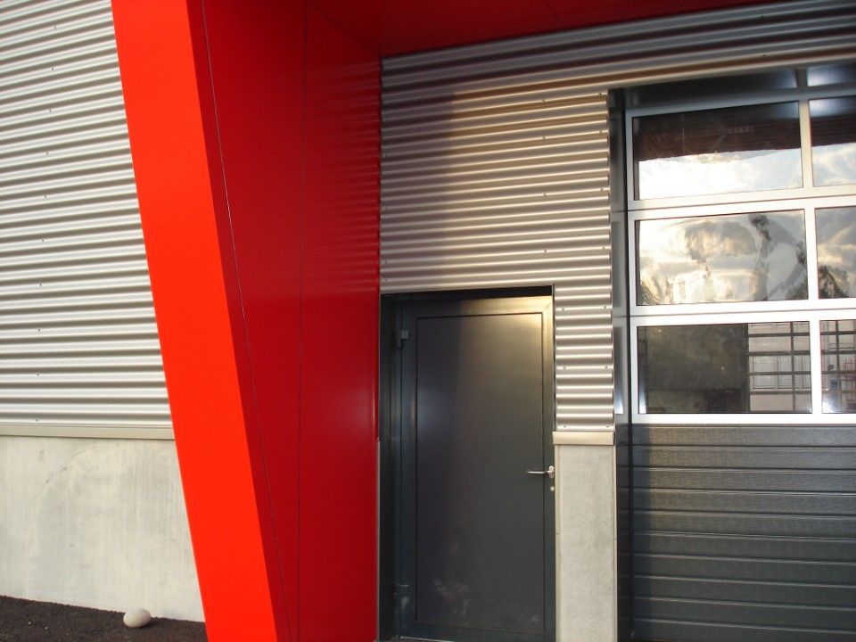Roter Stützbalken, graue Fassadenverkleidung, schwarze Tür und Garagentor.