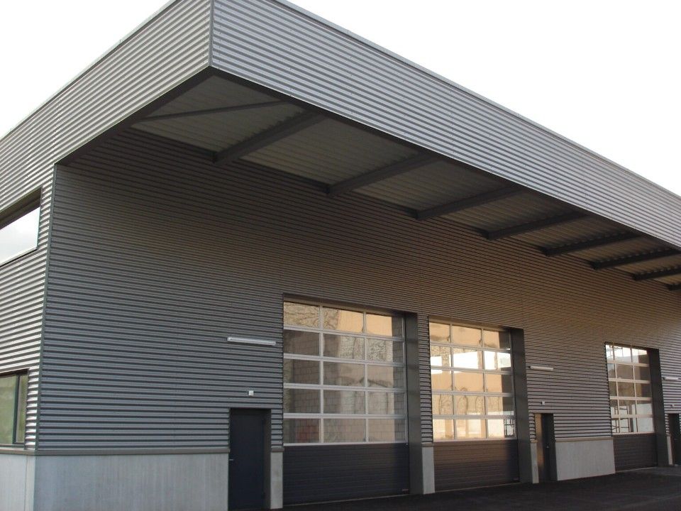 Graues Industriegebäude mit Wellblechverkleidung, grossen Garagentoren und einer kleinen Tür.