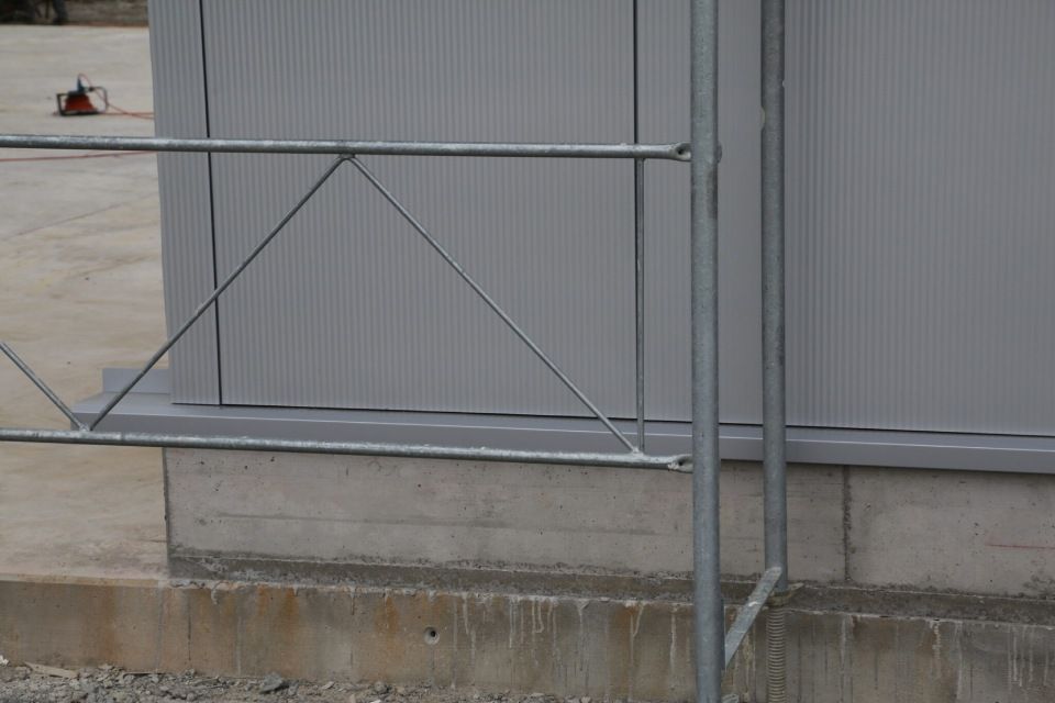 Metallgeländer neben einem grauen Gebäude mit Betonsockel, möglicherweise für eine Laderampe.