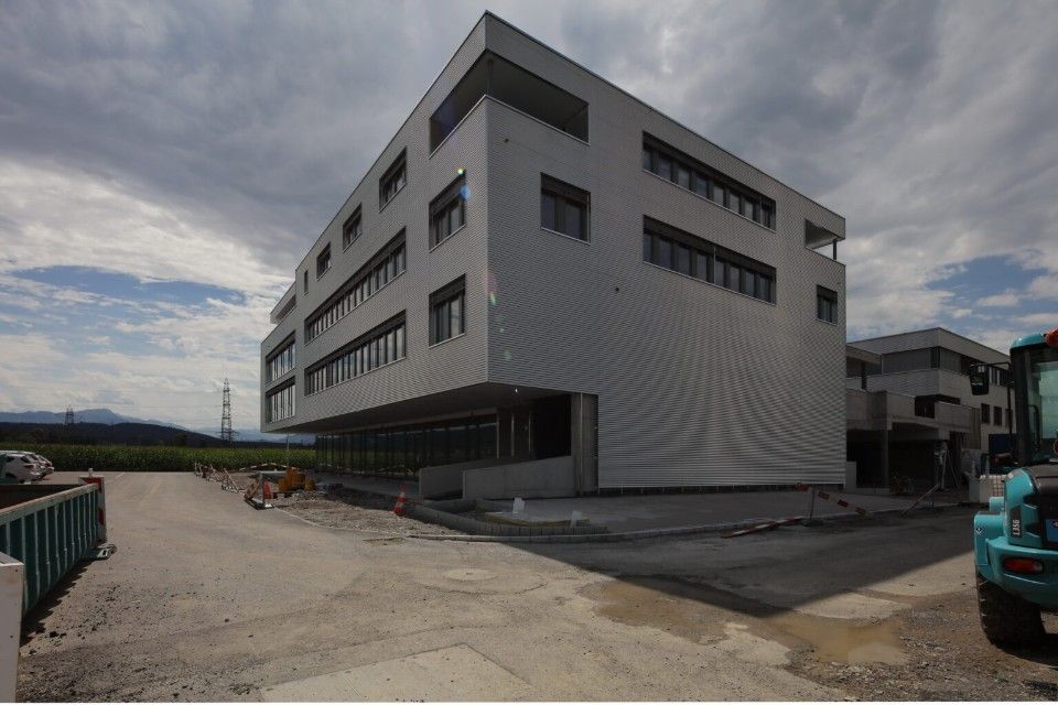 Modernes, mehrstöckiges Gebäude mit hellgrauer Fassade unter bewölktem Himmel, Bauarbeiten im Gange.