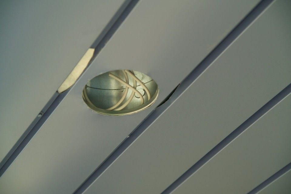 Eine metallene Schale mit eingravierten Mustern hängt von einer grauen Decke mit dunklen Balken herab.