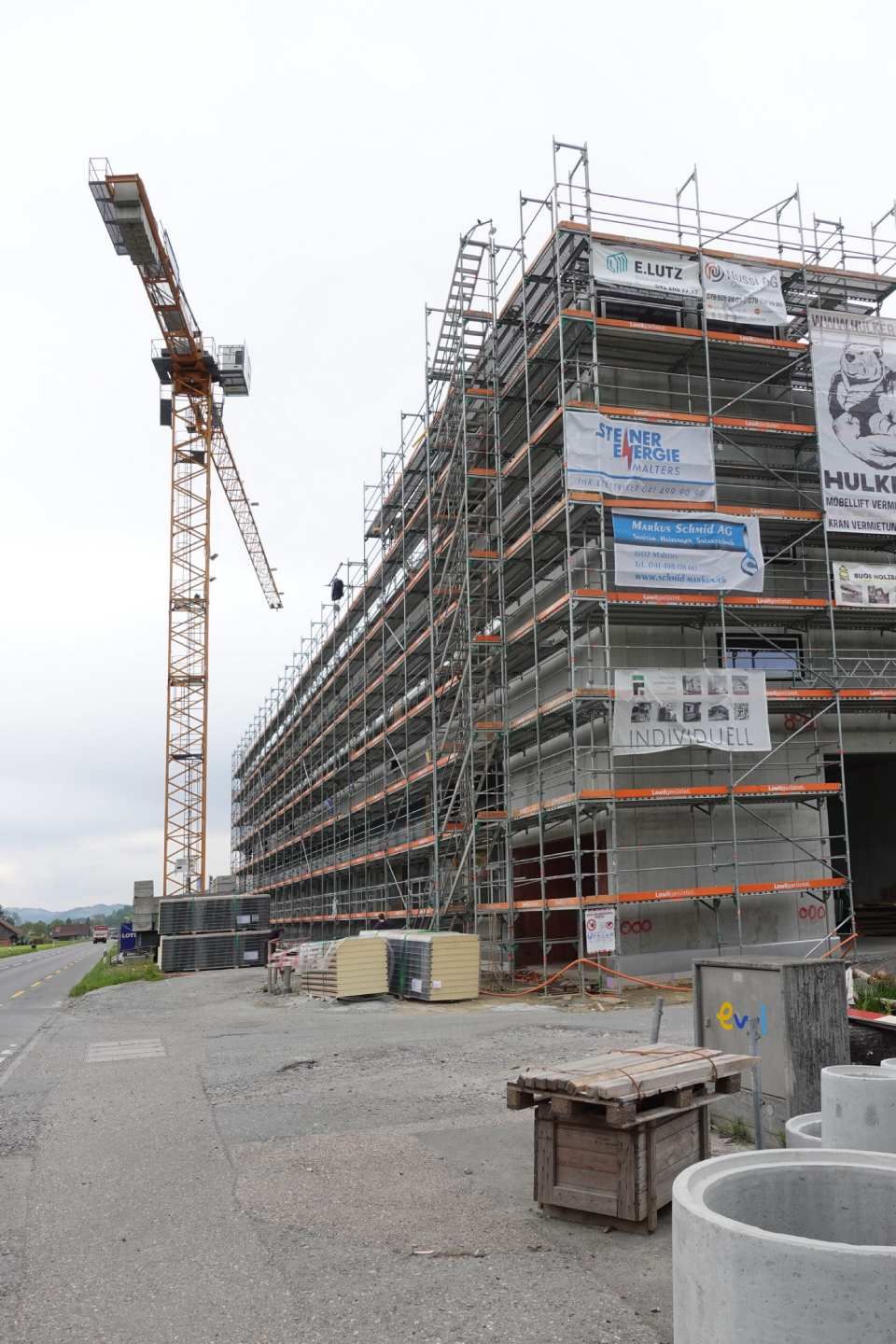 Baustelle mit einem hohen Kran neben einem mehrstöckigen, eingerüsteten Gebäude.