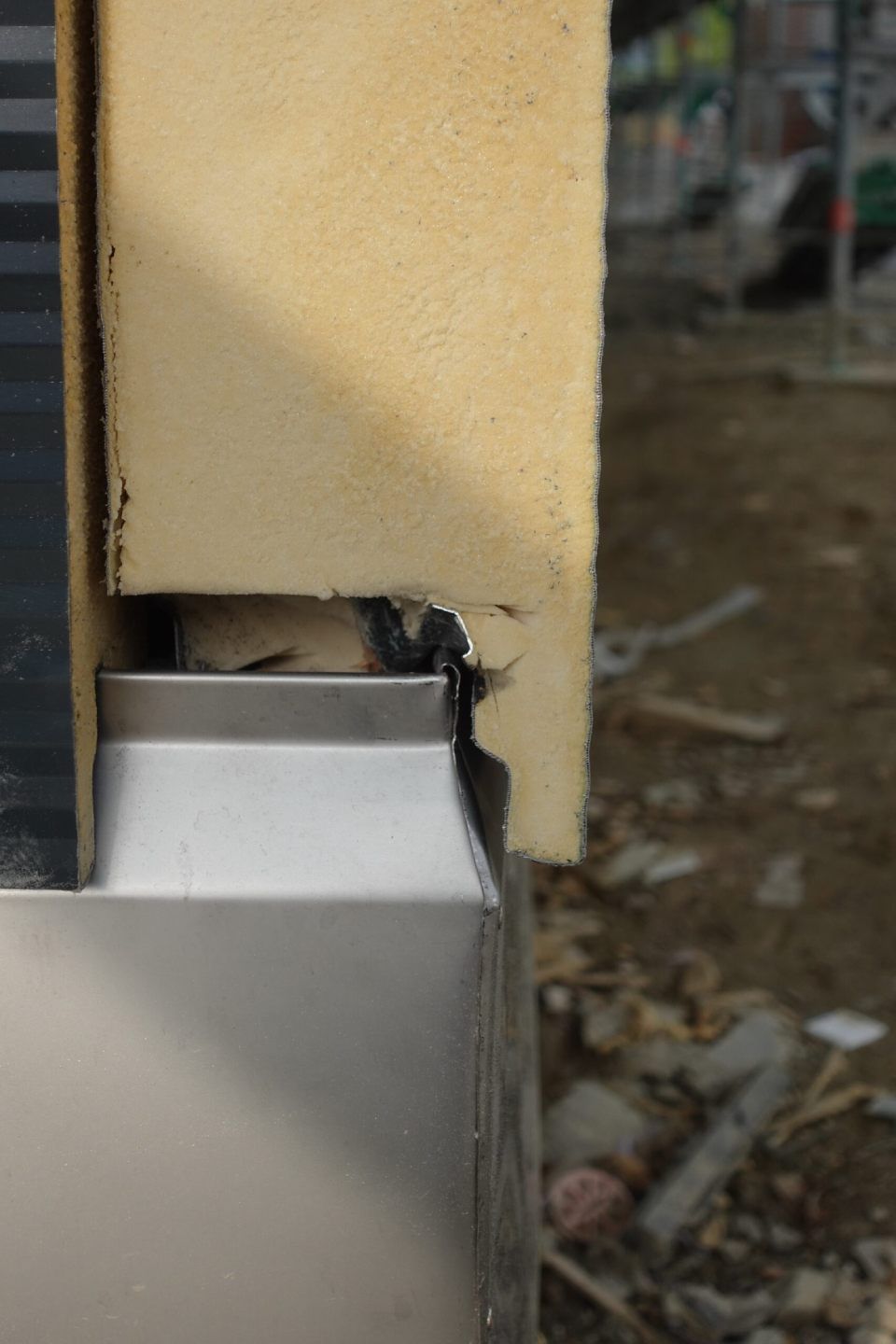Nahaufnahme einer Gebäudeecke, die Dämmung, Metallrahmen und eine Lücke zeigt, wahrscheinlich auf einer Baustelle.