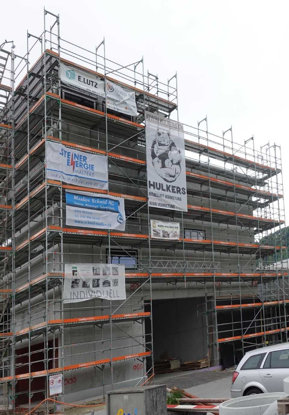 Das Gebäude befindet sich im Bau und ist von einem Gerüst umgeben, an dem mehrere Banner angebracht sind.