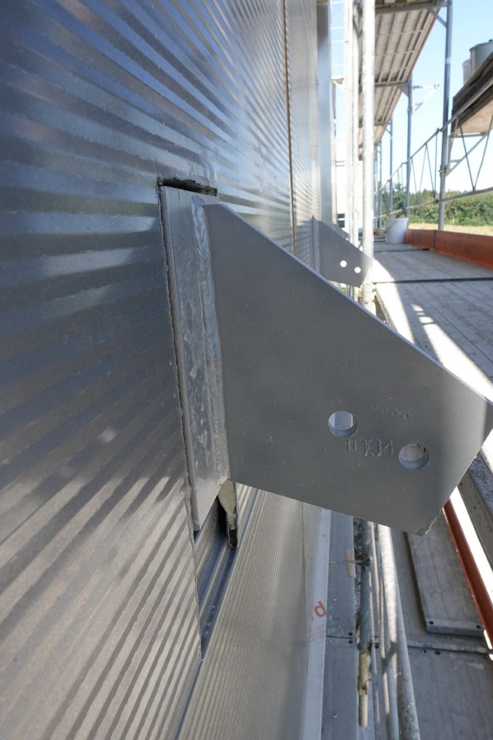 An der Aussenfassade eines Gebäudes sind Metallhalterungen befestigt; im Hintergrund ist ein Gerüst zu sehen.