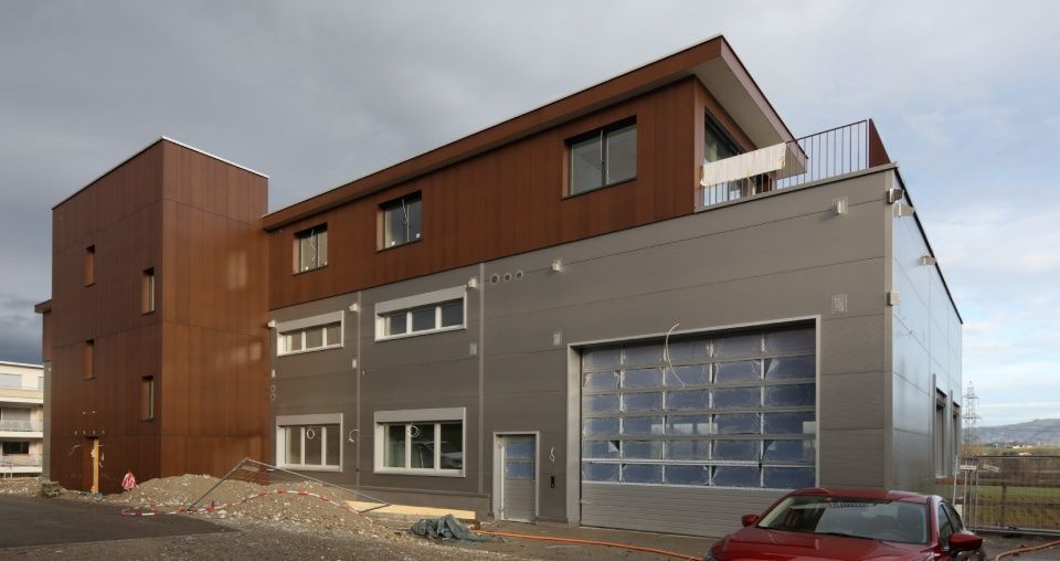 Modernes Gebäude mit braunen und grauen Paneelen, Garagentor und kleinem roten Auto.