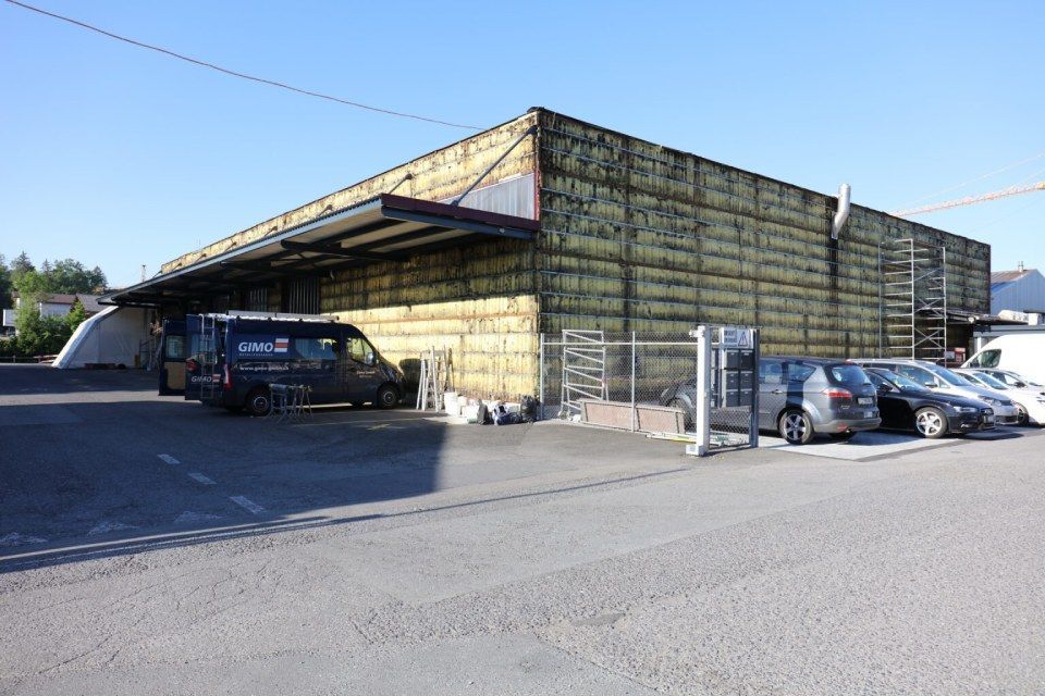 Gebäude mit freiliegender Dämmung, geparkten Autos und einem Lieferwagen auf Asphalt.