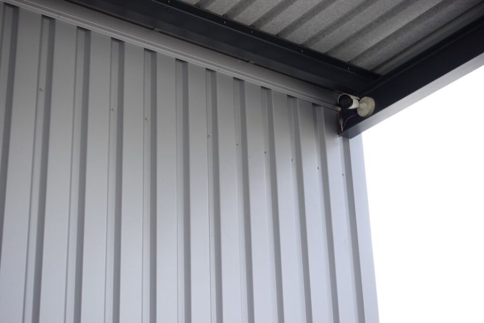 Graue Wellblechwand und -dach. Schwarzer Metallträger und weisser Himmel.