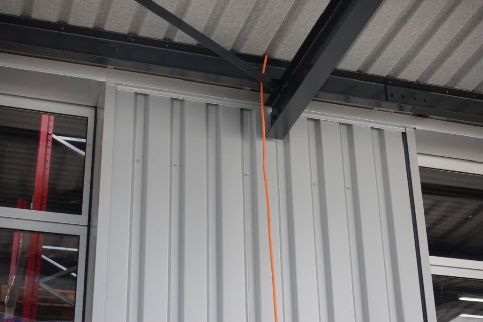 Äusseres Gebäude mit grauer Metallverkleidung und orangefarbenem Kabel, das vom Dach herabhängt.