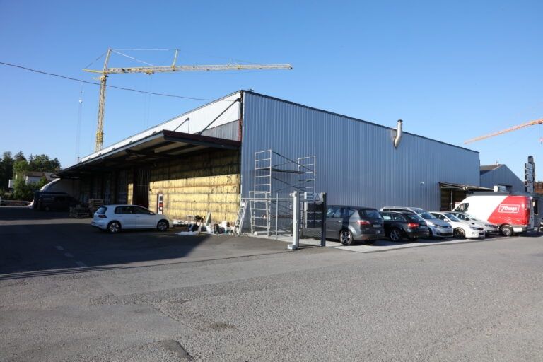 Lagerhalle mit geparkten Autos, Baukran und Gerüst.