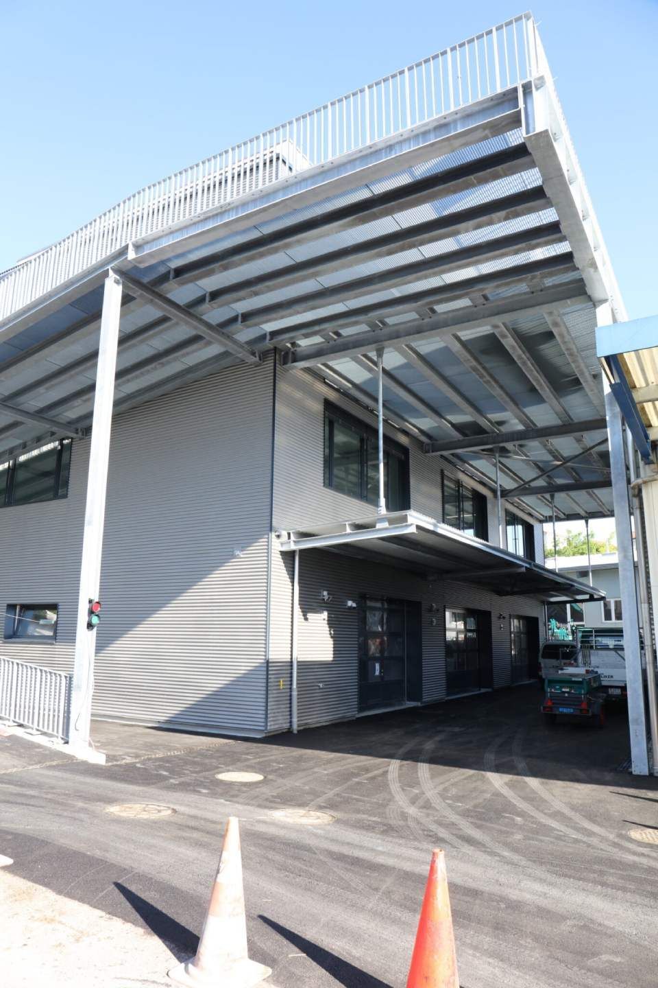 Zweistöckiges Gebäude mit grauer Fassadenverkleidung und Metalldach/Markise, geparktes Auto, orangefarbene Verkehrskegel.