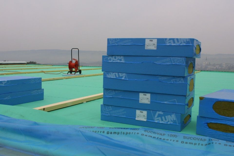 Blaue Dämmblöcke sind auf einem Gründach gestapelt. Ein Karren und in der Ferne sind Berge zu sehen.