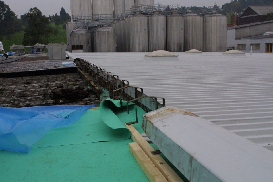 Das Dach eines Gebäudes während der Bauphase, auf dem blaue Planen und Baumaterialien zu sehen sind.