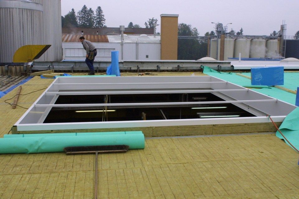 Dachkonstruktion mit Oberlichtrahmen, Dämmung und einem Arbeiter. Bewölkter Himmel.