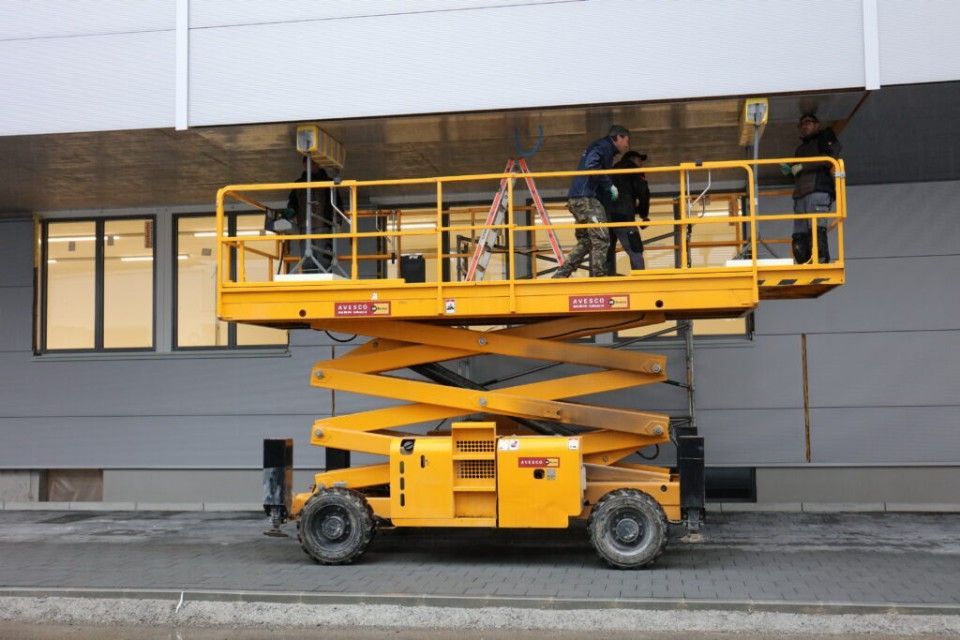 Gelbe Scherenbühne mit Arbeitern, die die Aussenfassade eines Gebäudes reparieren.