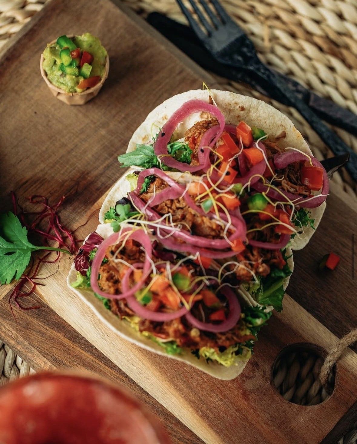 Sándwich abierto de verduras sobre tabla de madera con coloridos ingredientes rallados y hierbas aromáticas.