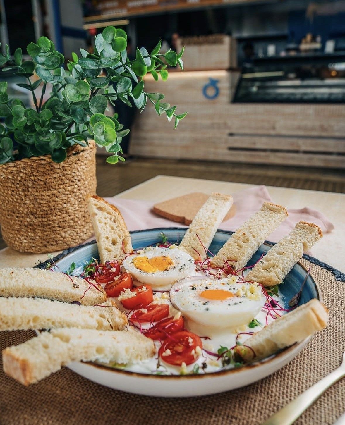Plato de tostadas con huevos pasados ​​por agua y tomates cherry sobre una mesa, junto a una planta en maceta.