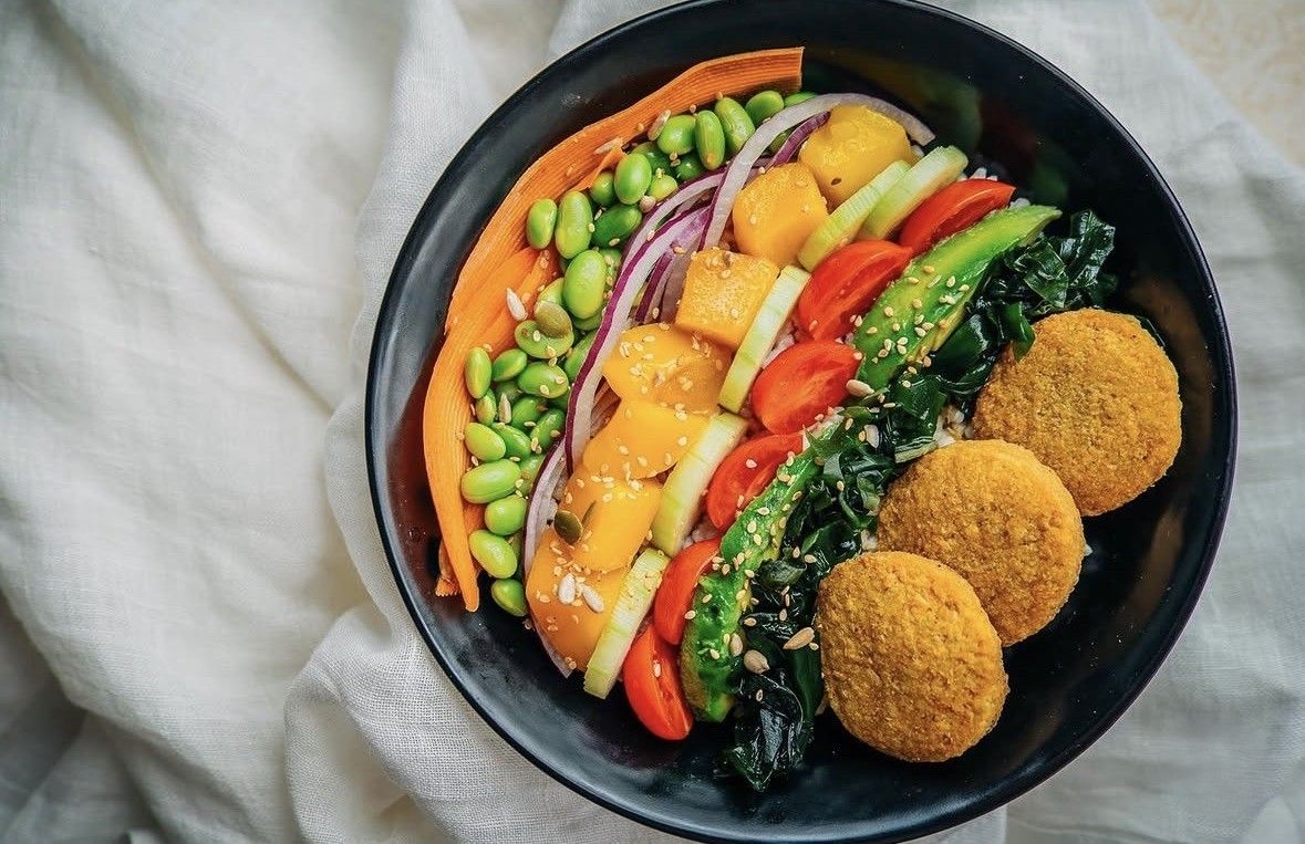 Bol de verduras colorido con falafel, verduras en rodajas, aguacate, edamame y hojas verdes en un bol negro.