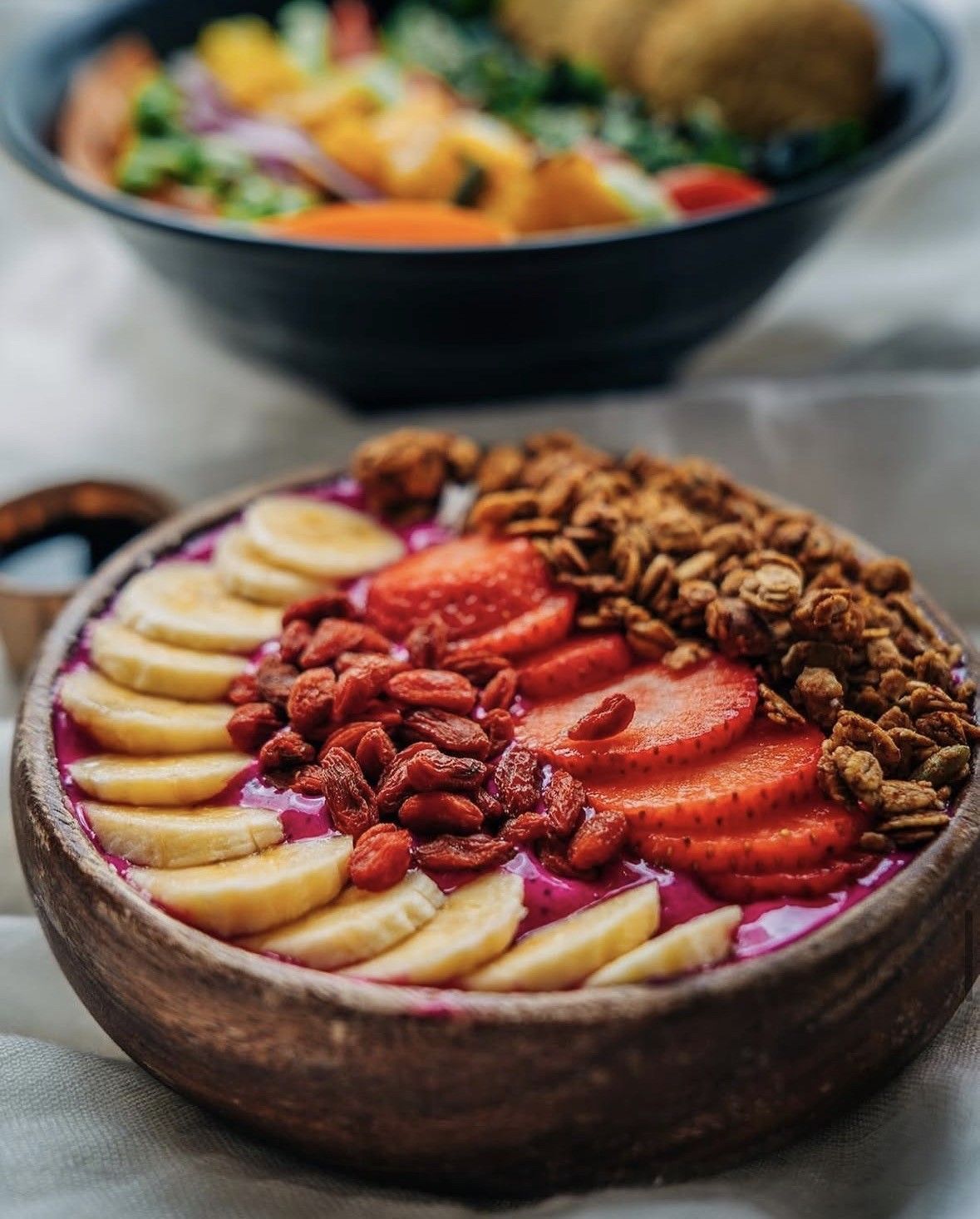 Bol de açaí con plátano, fresas, frutos rojos y granola en un bol de madera.