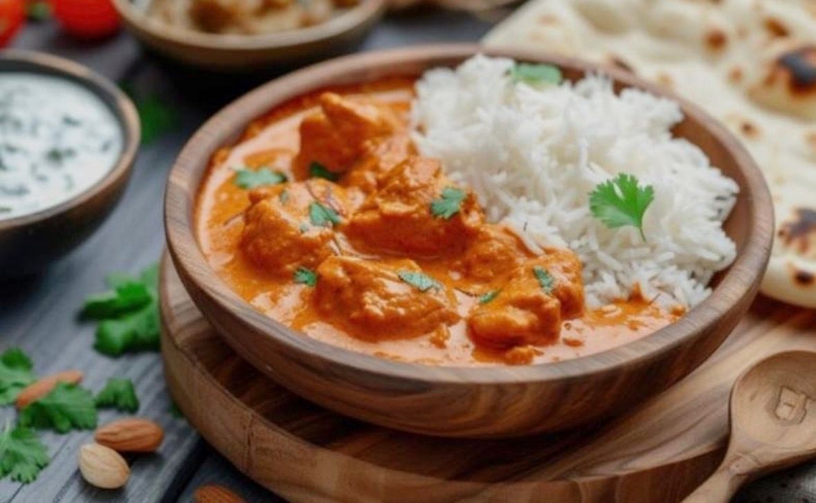 Curry cremoso de naranja con arroz blanco en un cuenco de madera, adornado con cilantro sobre una mesa rústica.