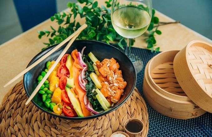 Ensalada colorida con aguacate, fruta y palitos de pan sobre una mesa rústica junto a una copa de vino blanco.