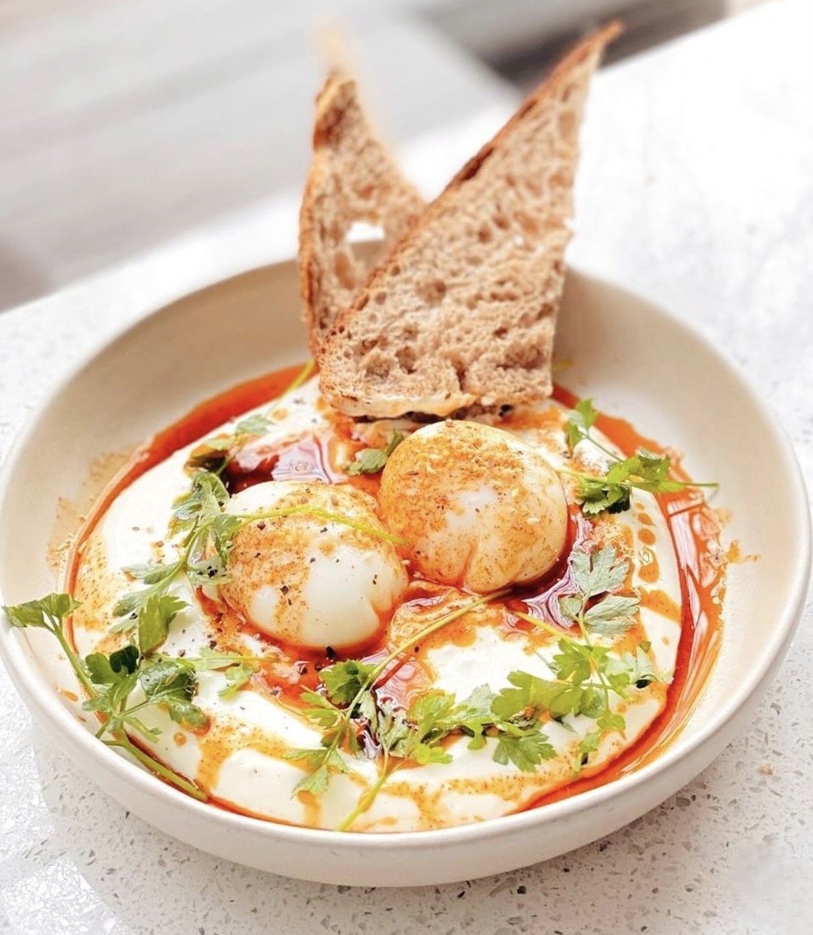 Tazón de sopa cremosa cubierto con huevos escalfados, hierbas, aceite de especias y triángulos de pan tostado.