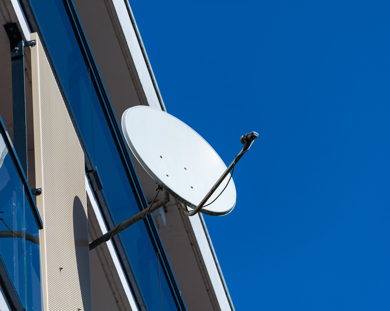Une antenne parabolique blanche est montée sur le côté d'un bâtiment contre un ciel bleu.