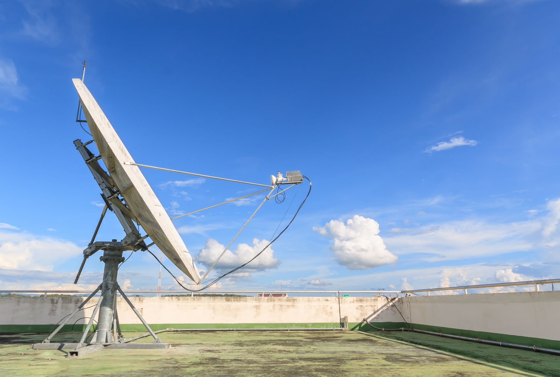 Antenne parabolique sur un toit, blanche sur fond de paysage urbain flou.
