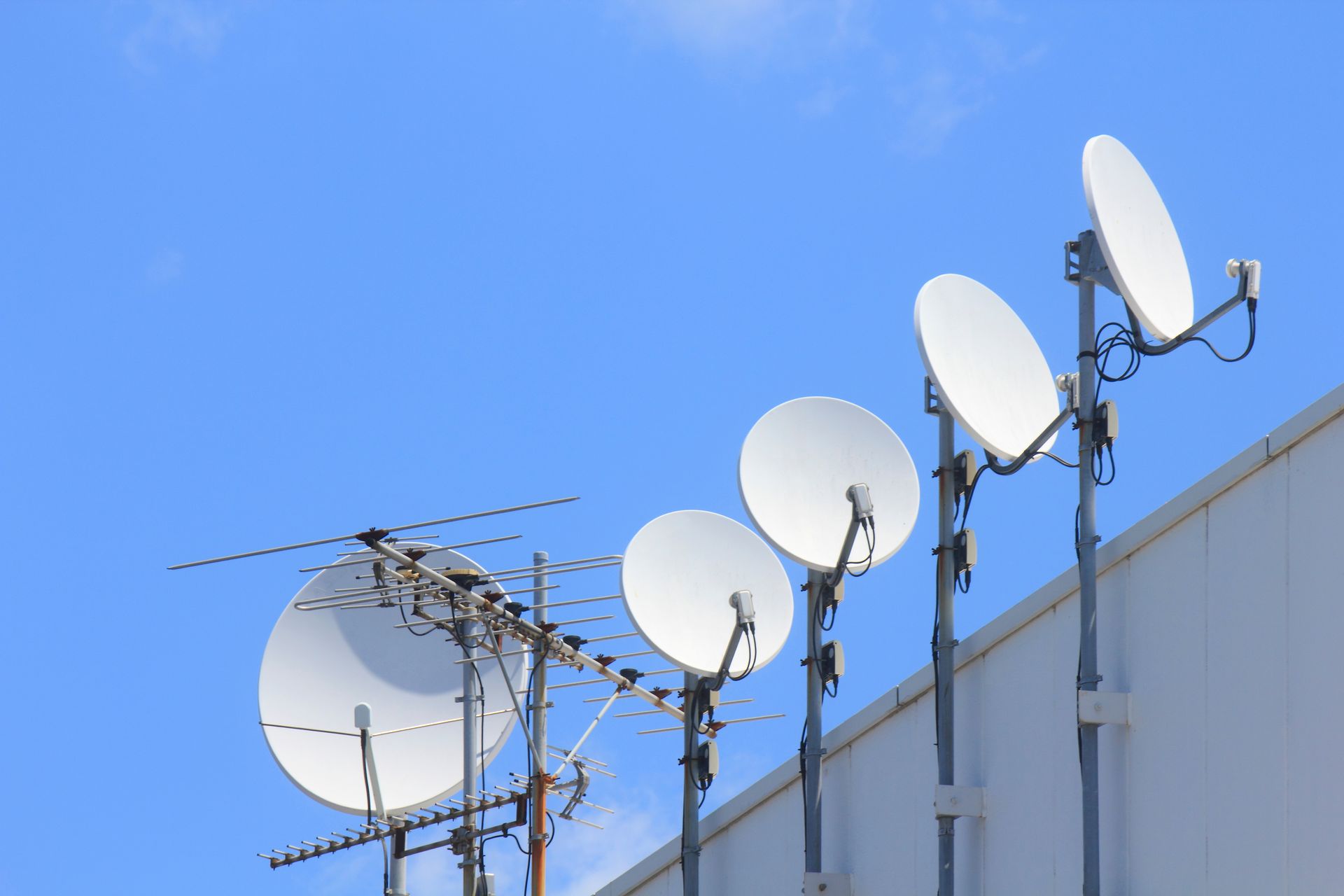 Réseau d'antennes paraboliques et d'une antenne sur le côté d'un bâtiment, contre un ciel bleu.