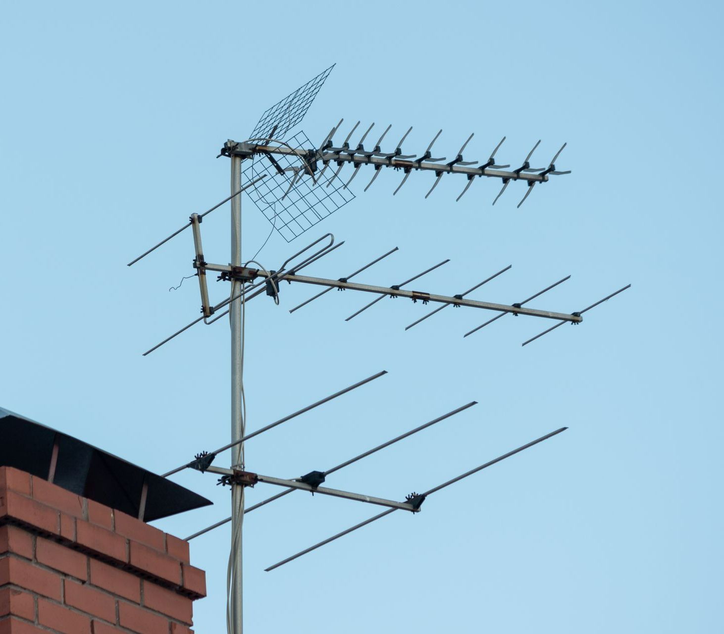 Antenne TV montée sur une cheminée, avec plusieurs tiges métalliques horizontales et inclinées contre un ciel bleu clair.