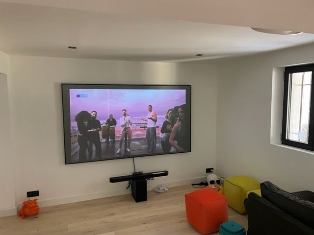 Téléviseur monté sur un mur marron au-dessus d'un comptoir blanc dans une pièce, avec des objets décoratifs à proximité.