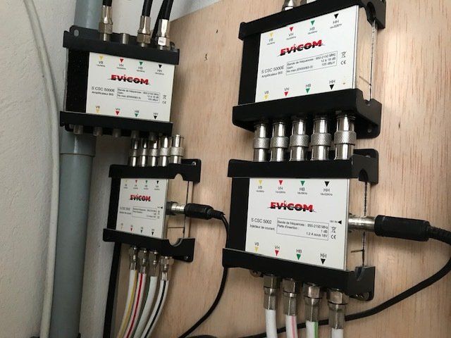 Quatre répartiteurs de câbles montés sur un panneau en bois, avec plusieurs connexions de câbles coaxiaux.