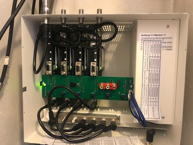 Une boîte blanche contenant des composants électroniques. Elle comprend un circuit imprimé vert, des câbles et des connecteurs.