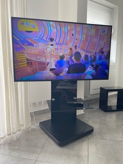 Téléviseur monté sur un support noir ; petit meuble en bois à proximité.