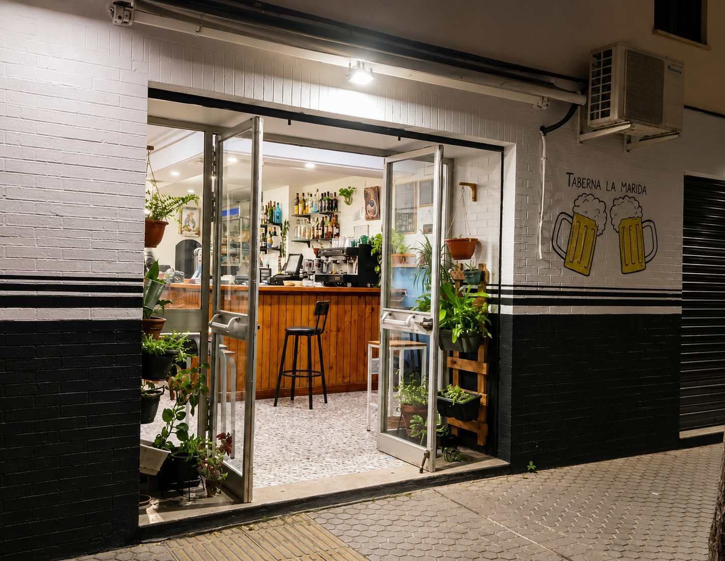 Escaparate de cristal abierto por la noche con un interior de cafetería iluminado con luz cálida, mostrador de madera.