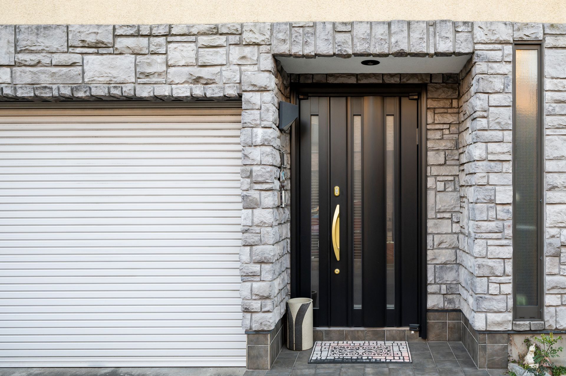 Porte d'entrée noire avec poignée dorée et façade en pierre.