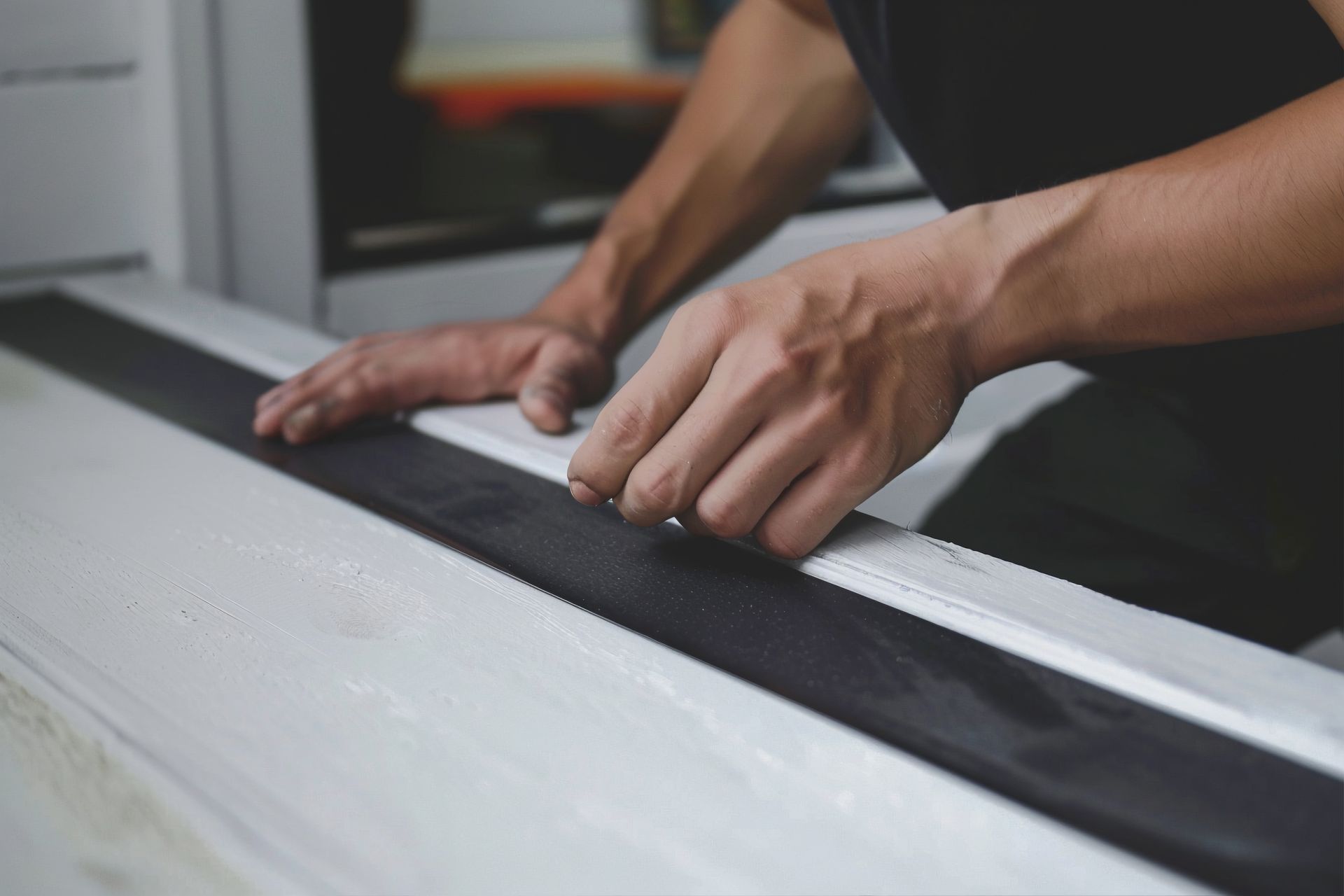 Personne utilisant ses mains pour installer un joint d'étanchéité noir sur une surface blanche.