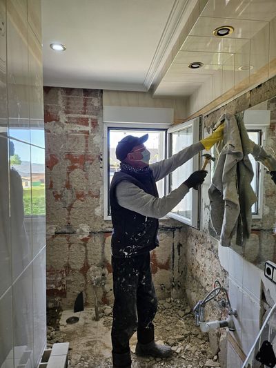 Un hombre está de pie en un baño sosteniendo un martillo.
