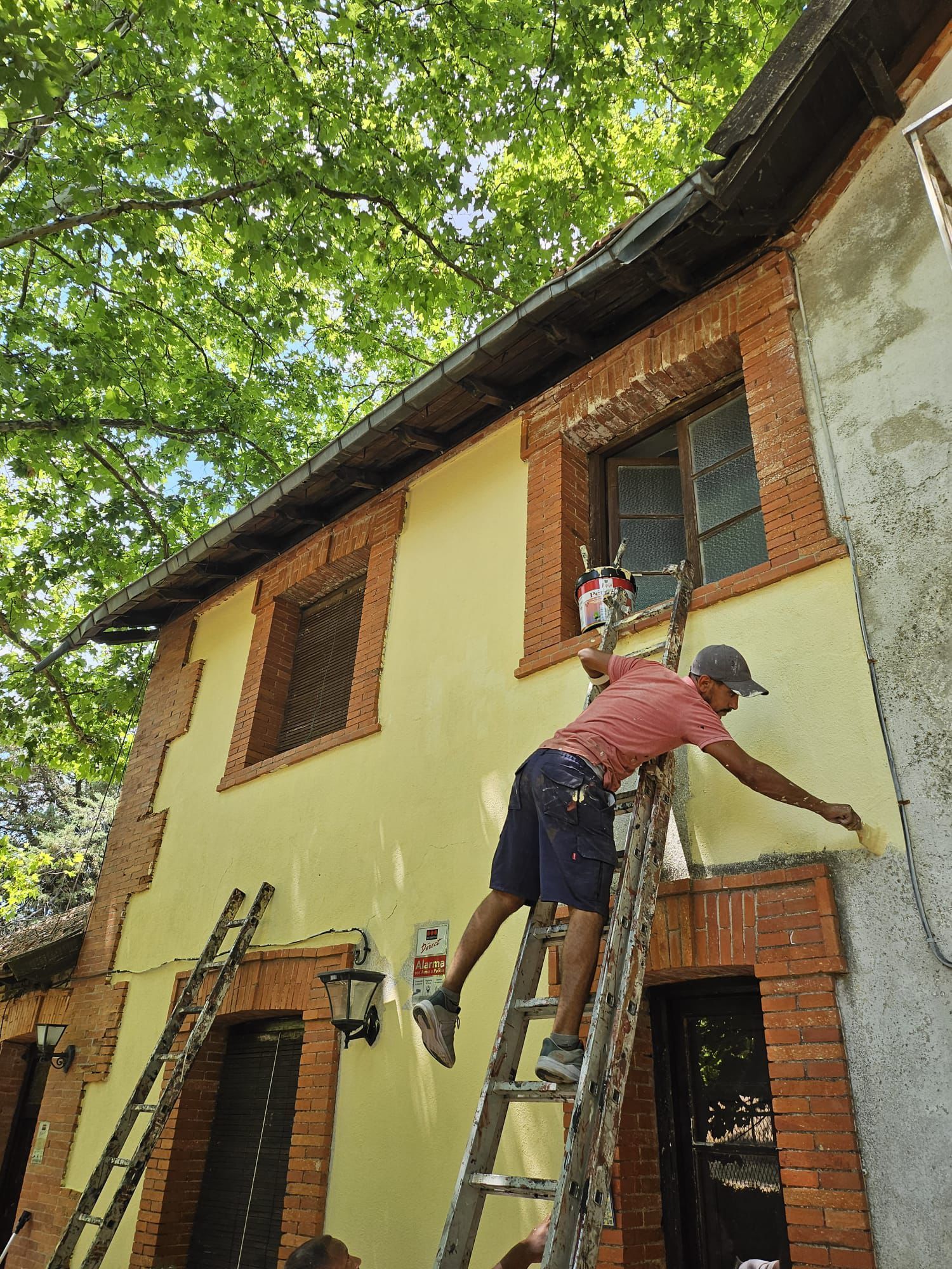 Un hombre está de pie en una escalera pintando el costado de un edificio.