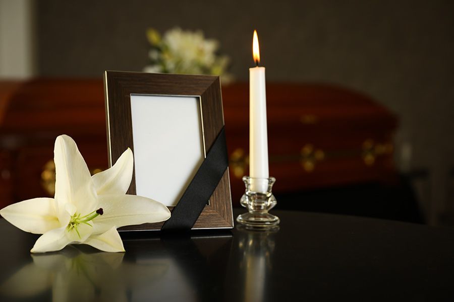 Un marco de fotos, una vela y una flor sobre una mesa delante de un ataúd.