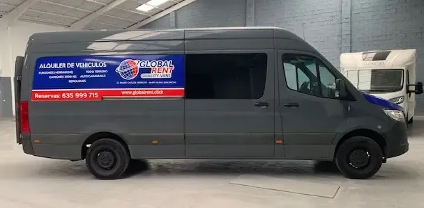 Furgoneta gris con logotipo estacionada en un almacén. Se ve otro vehículo al fondo.