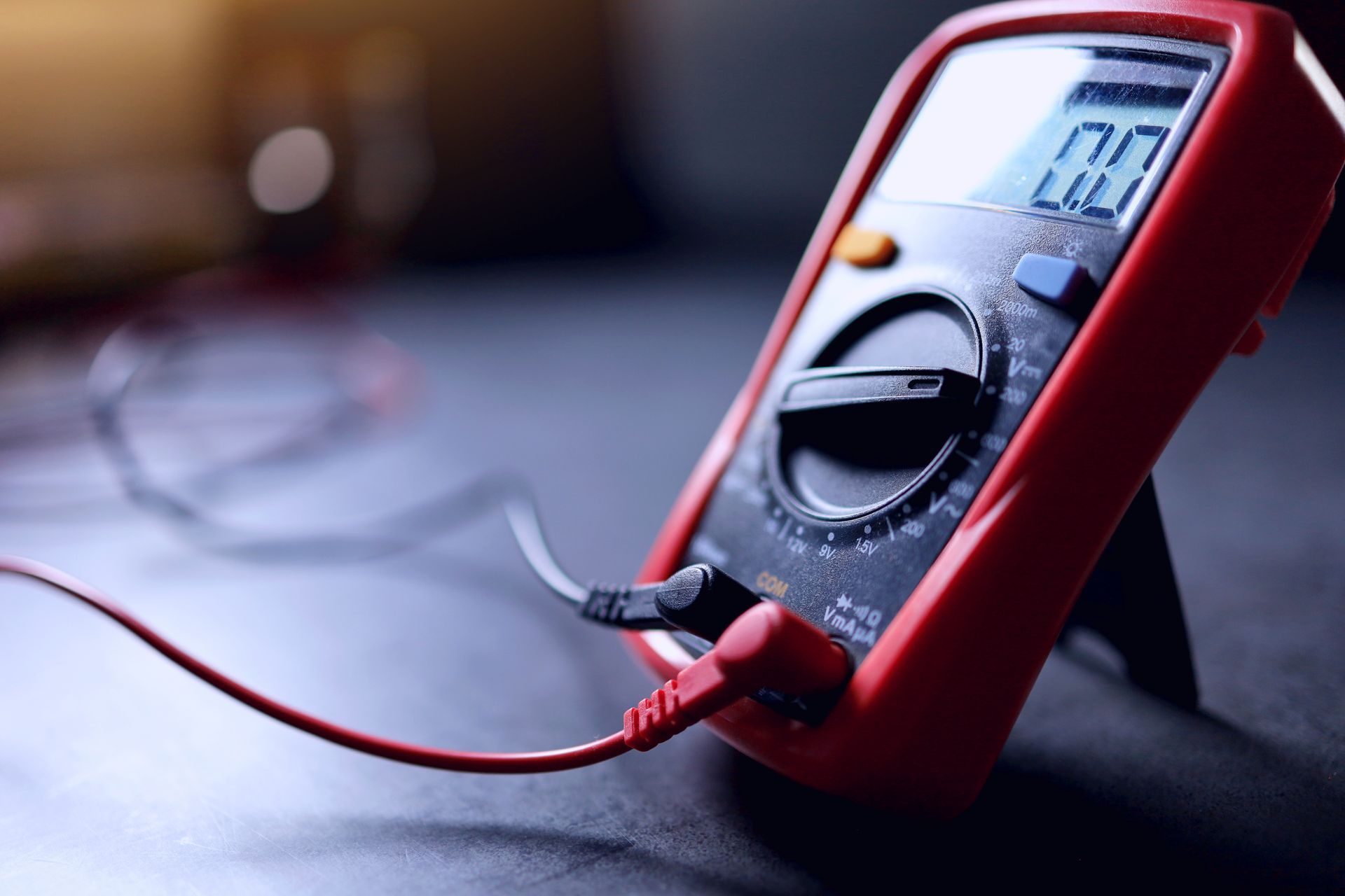 Handmultimeter mit roten und schwarzen Messspitzen in einer behandschuhten Hand an einem Arbeitsplatz