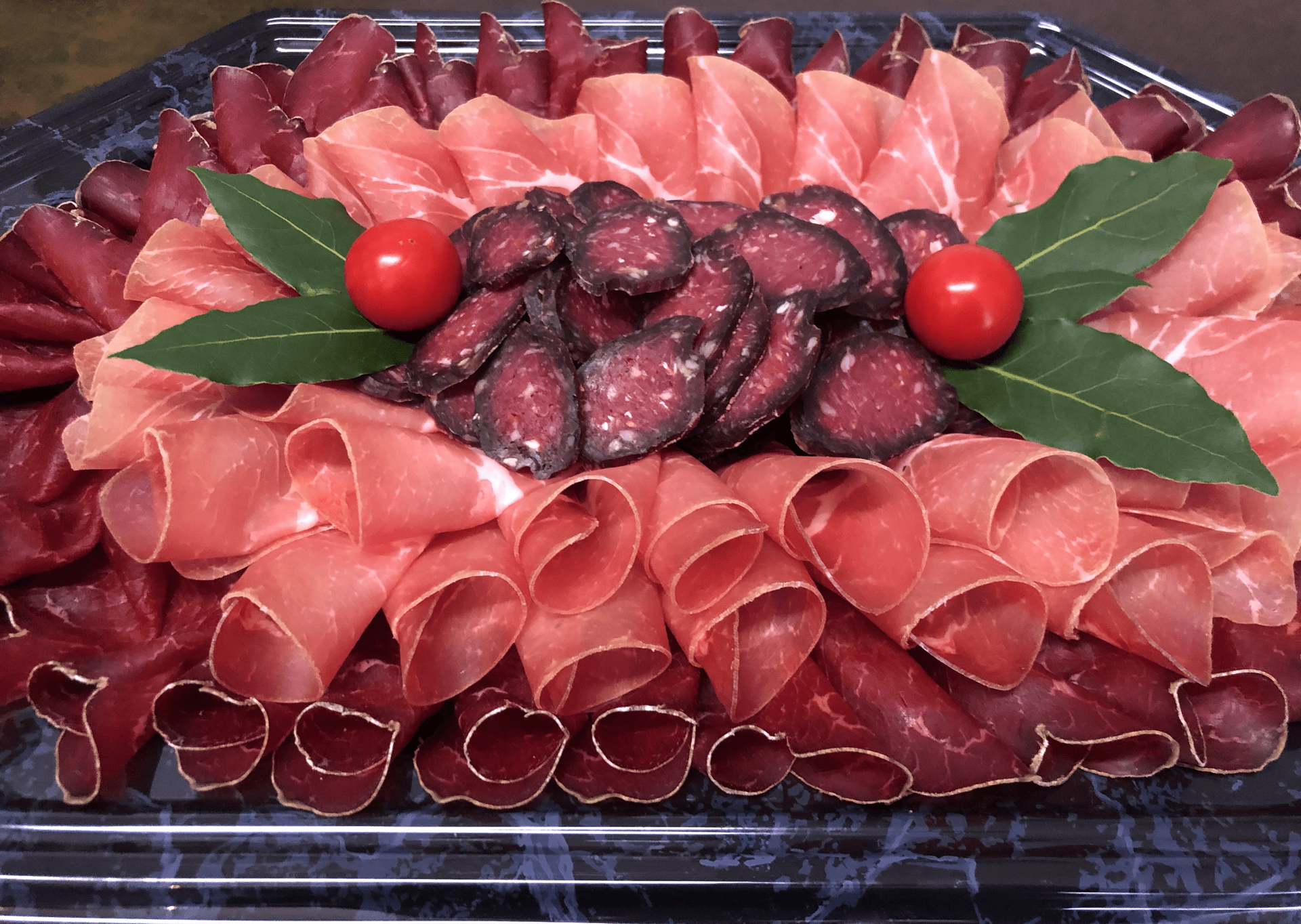 Un plateau de viandes avec des tomates et des feuilles vertes sur une table.