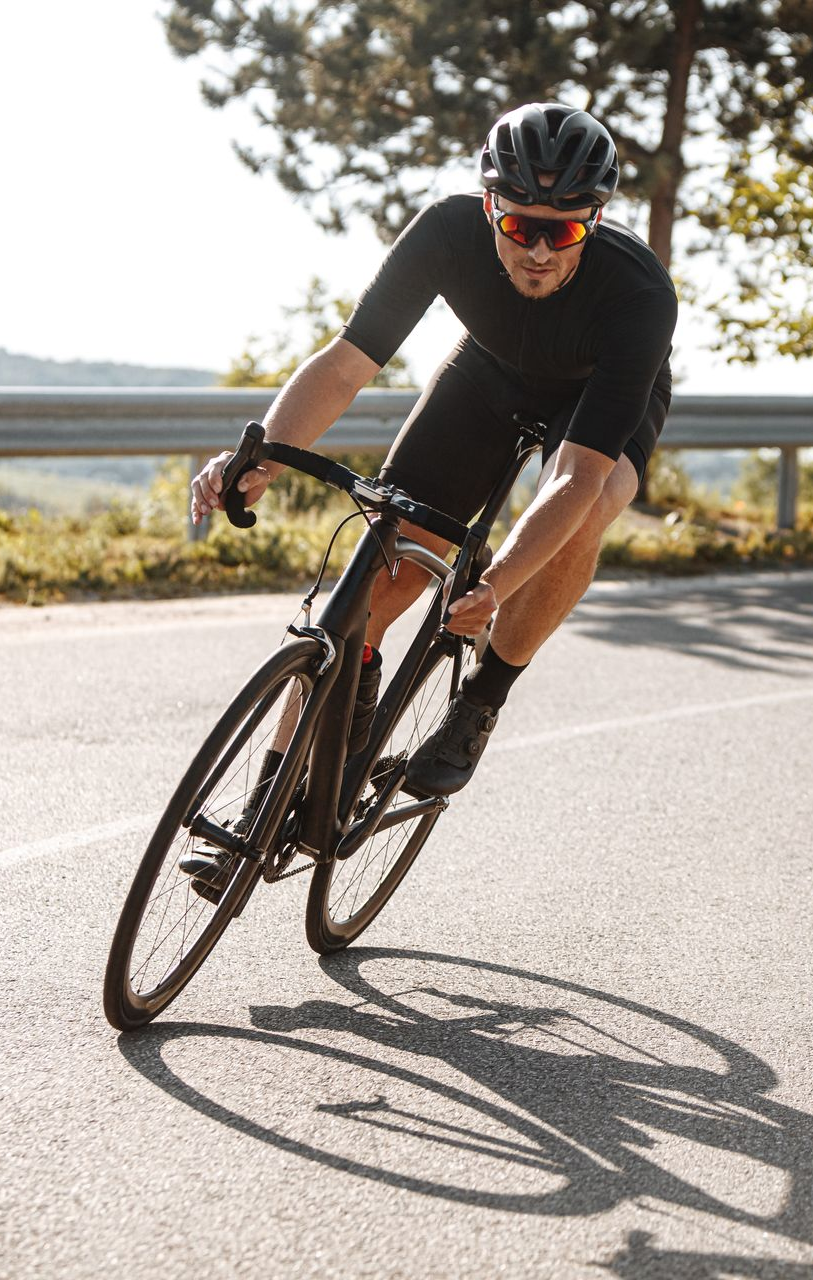 Un cycliste en tenue noire se penche dans un virage, son ombre se projetant sur la chaussée.