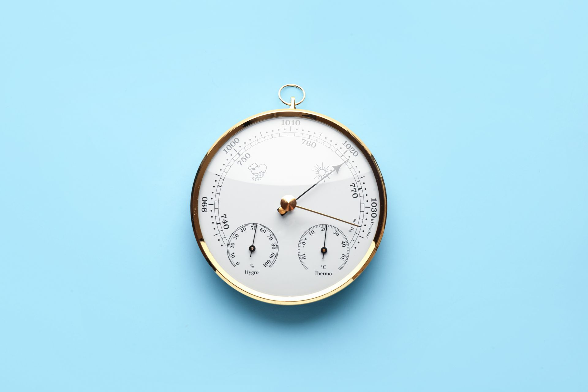 Un baromètre à cerclage en laiton sur fond bleu clair, affichant différentes indications.